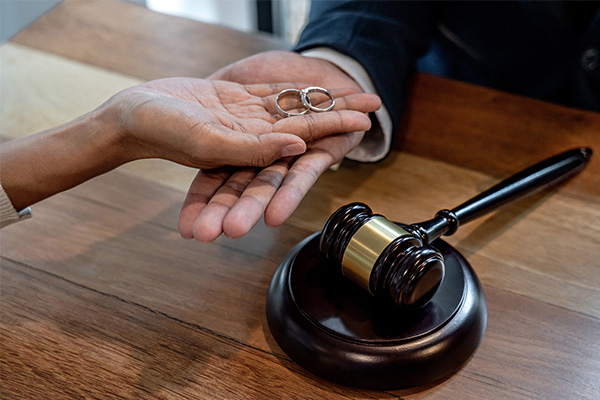 Hands holding wedding rings over desk with gavel representing Divorce